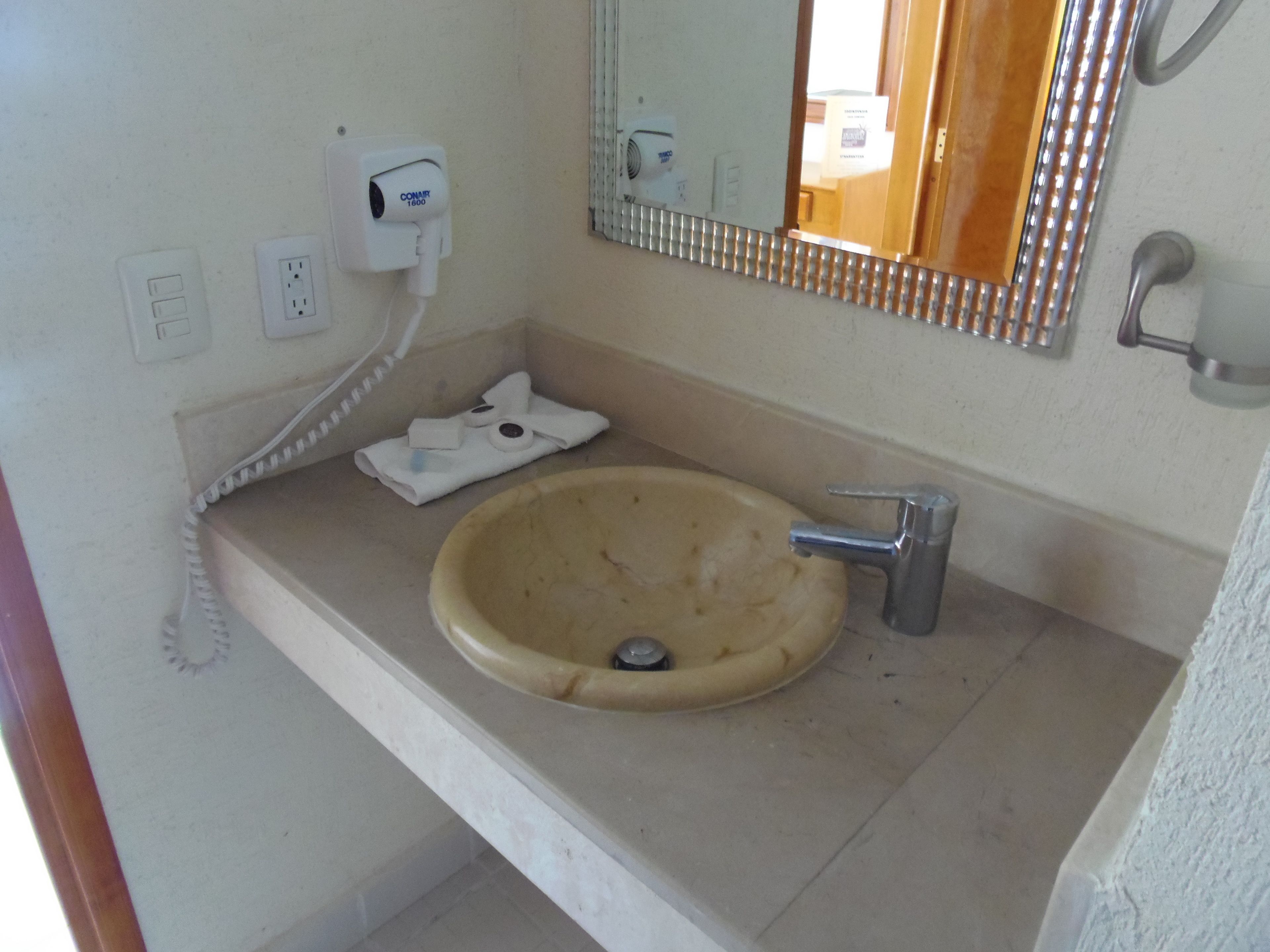 Ein Badezimmer mit einem beigefarbenem Waschbecken, einem Spiegel, einem Handtuch und einem Telefon.