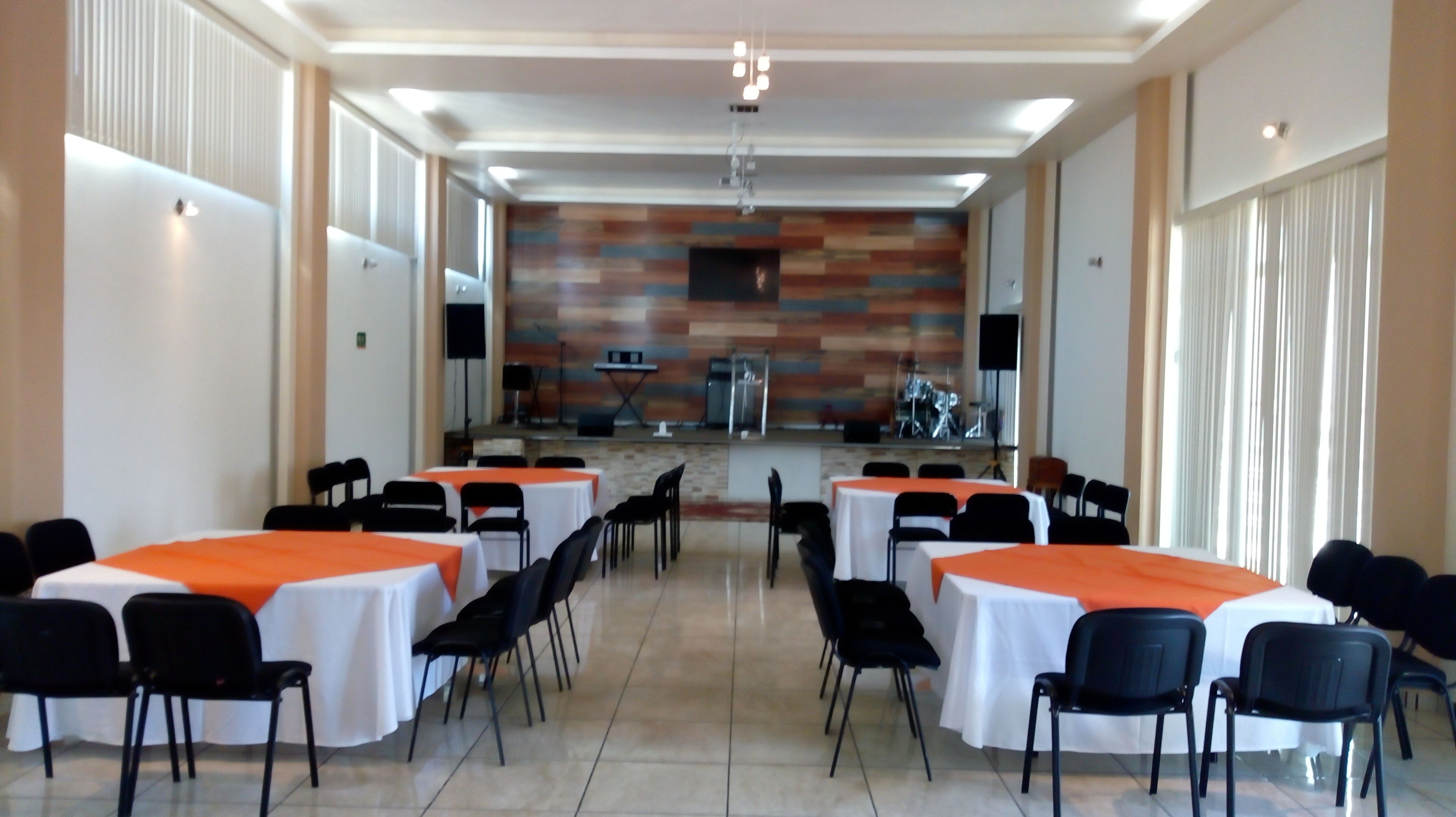 A conference room with tables and chairs, a stage with musical instruments, and a large window with curtains.