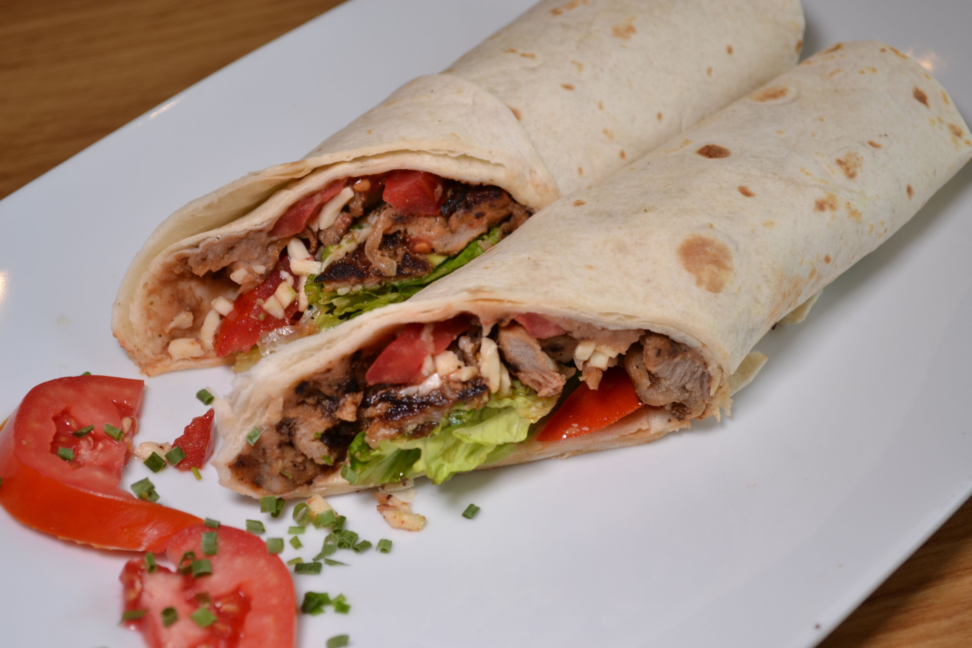 Un burrito garni de viande, de laitue et de tomates, servi sur une assiette blanche.