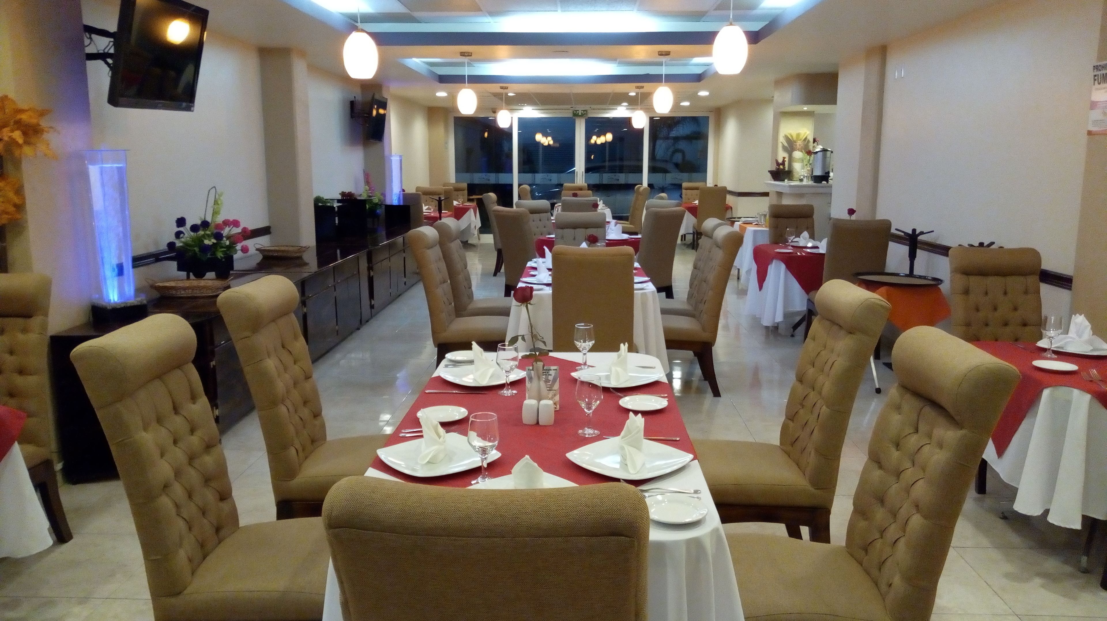 A restaurant with a long table set for dining, multiple chairs, and a television mounted on the wall.