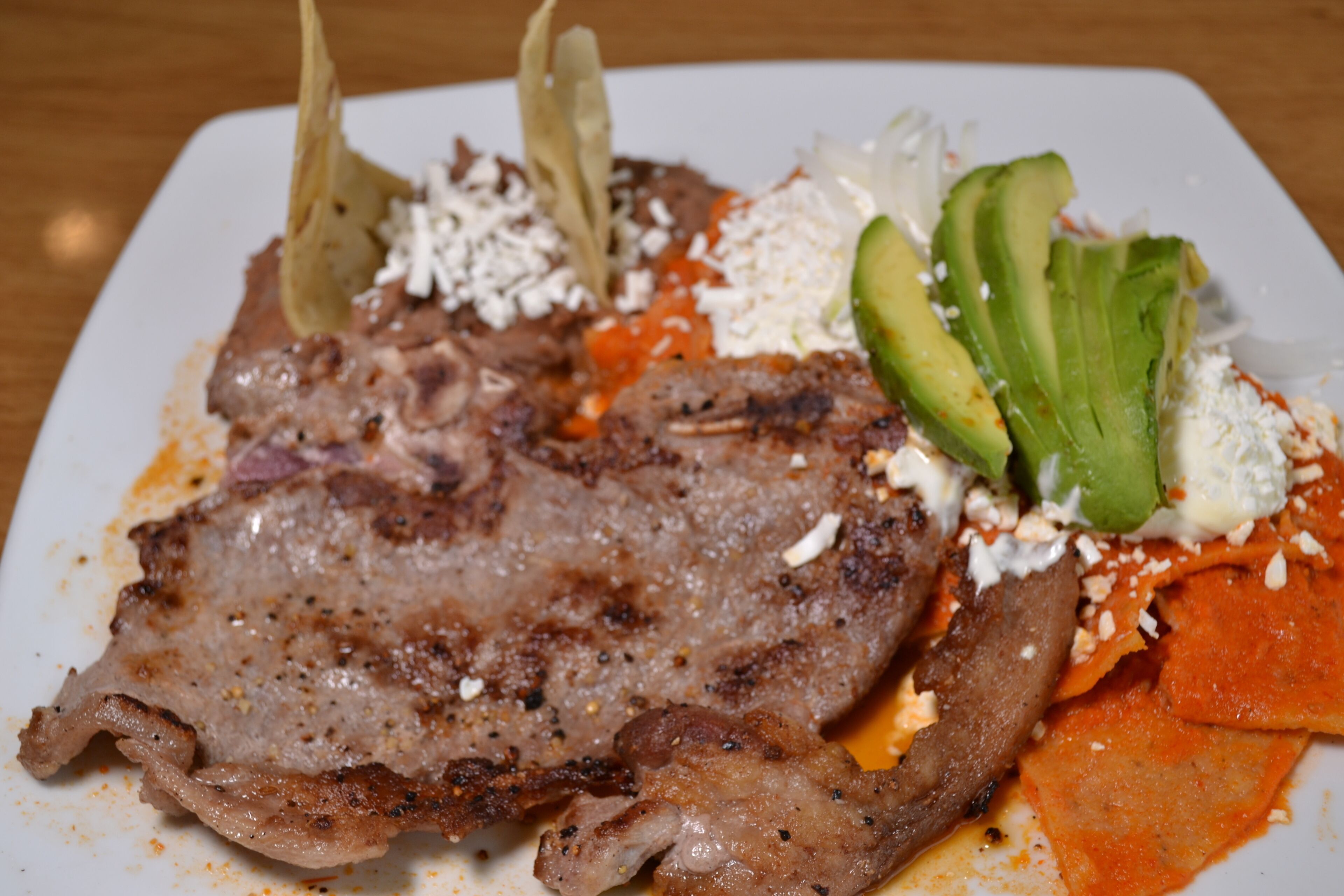 Un plato con carne a la parrilla, aguacate, queso y salsa roja.