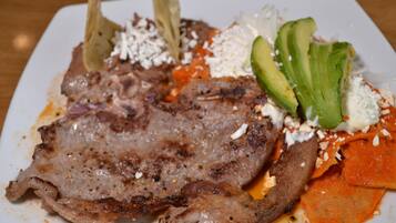 Un plato con carne a la parrilla, aguacate, queso y salsa roja.
