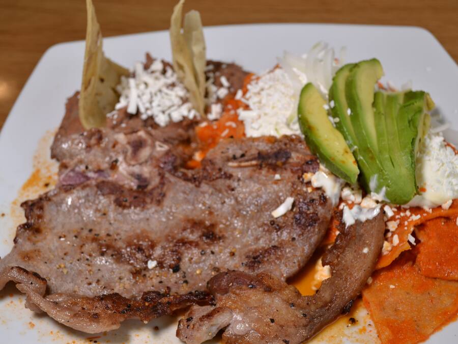 A plate with grilled meat, avocado, cheese, and a red sauce.
