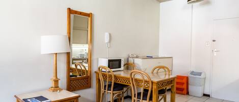 Habitación compacta con mesa de comedor, sillas, microondas, lámpara, espejo y cubo de basura.