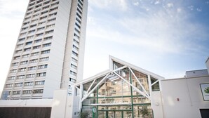 A modern building with a glass facade and a geometric design, adjacent to a tall residential building. - Gardens Centre Holiday Apartments (Cape Town)