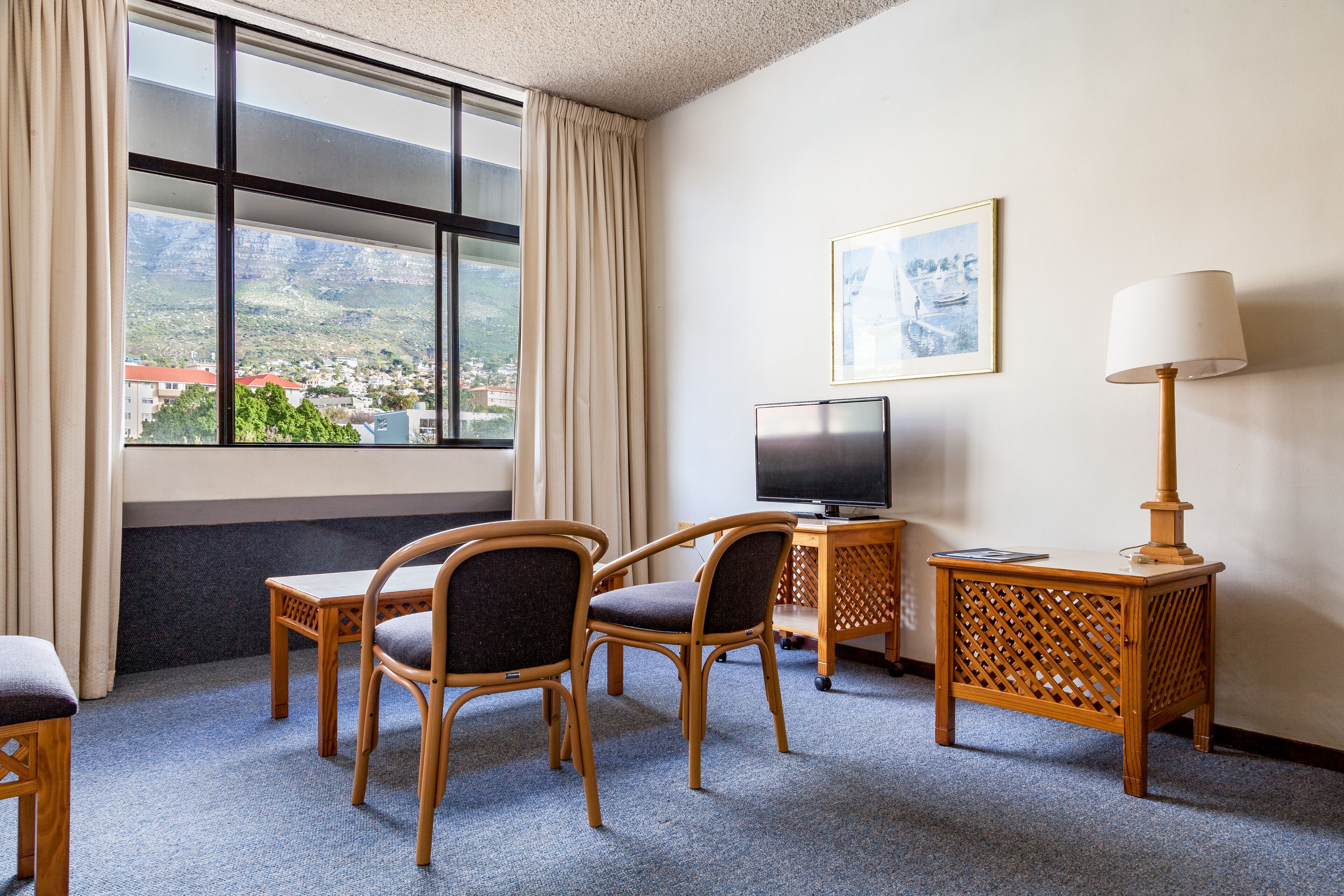 Habitación de hotel con un ventanal grande, dos sillas, una mesita, un televisor y una lámpara.