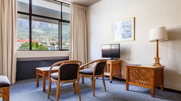 A hotel room with a large window, two chairs, a small table, a TV, and a lamp.