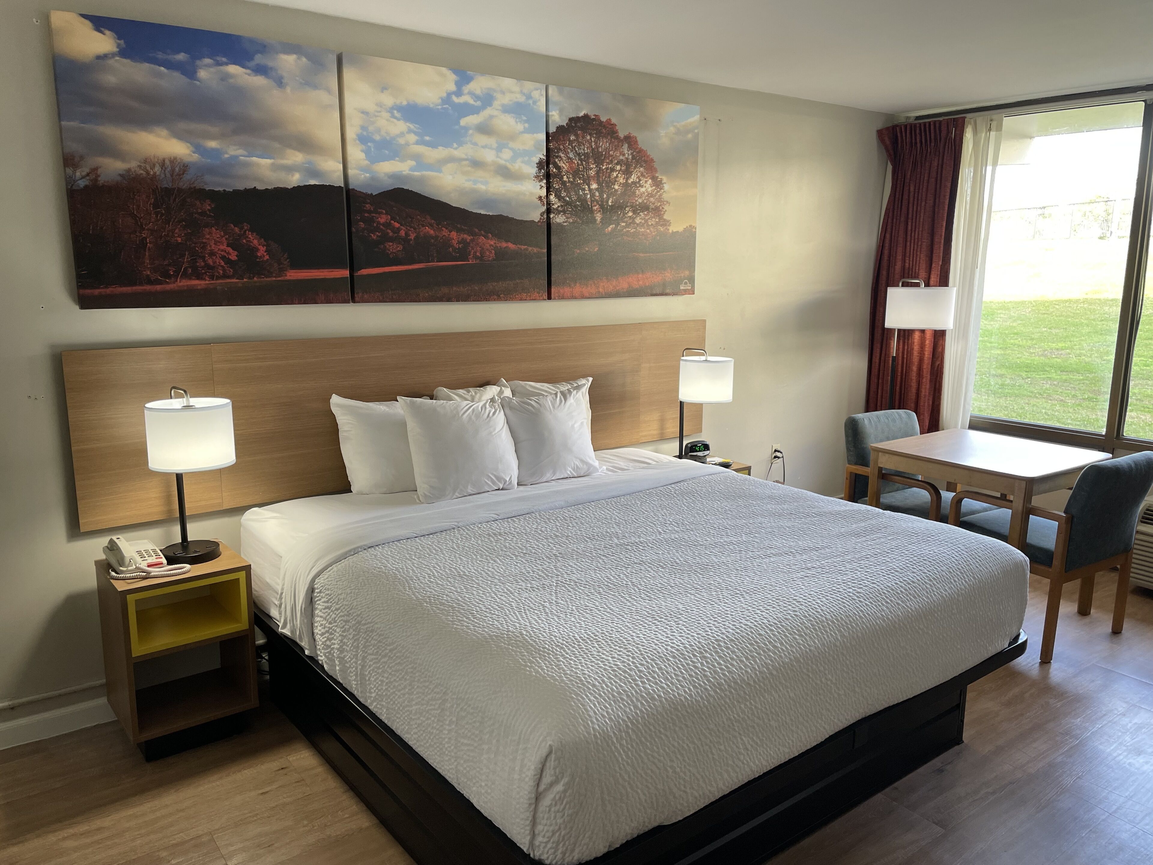 A hotel room with a large bed, bedside lamps, a desk, and a window with curtains.