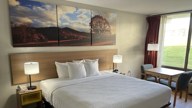 A hotel room with a large bed, bedside lamps, a desk, and a window with curtains. - Days Inn by Wyndham Valdosta/Near Valdosta Mall (Valdosta)