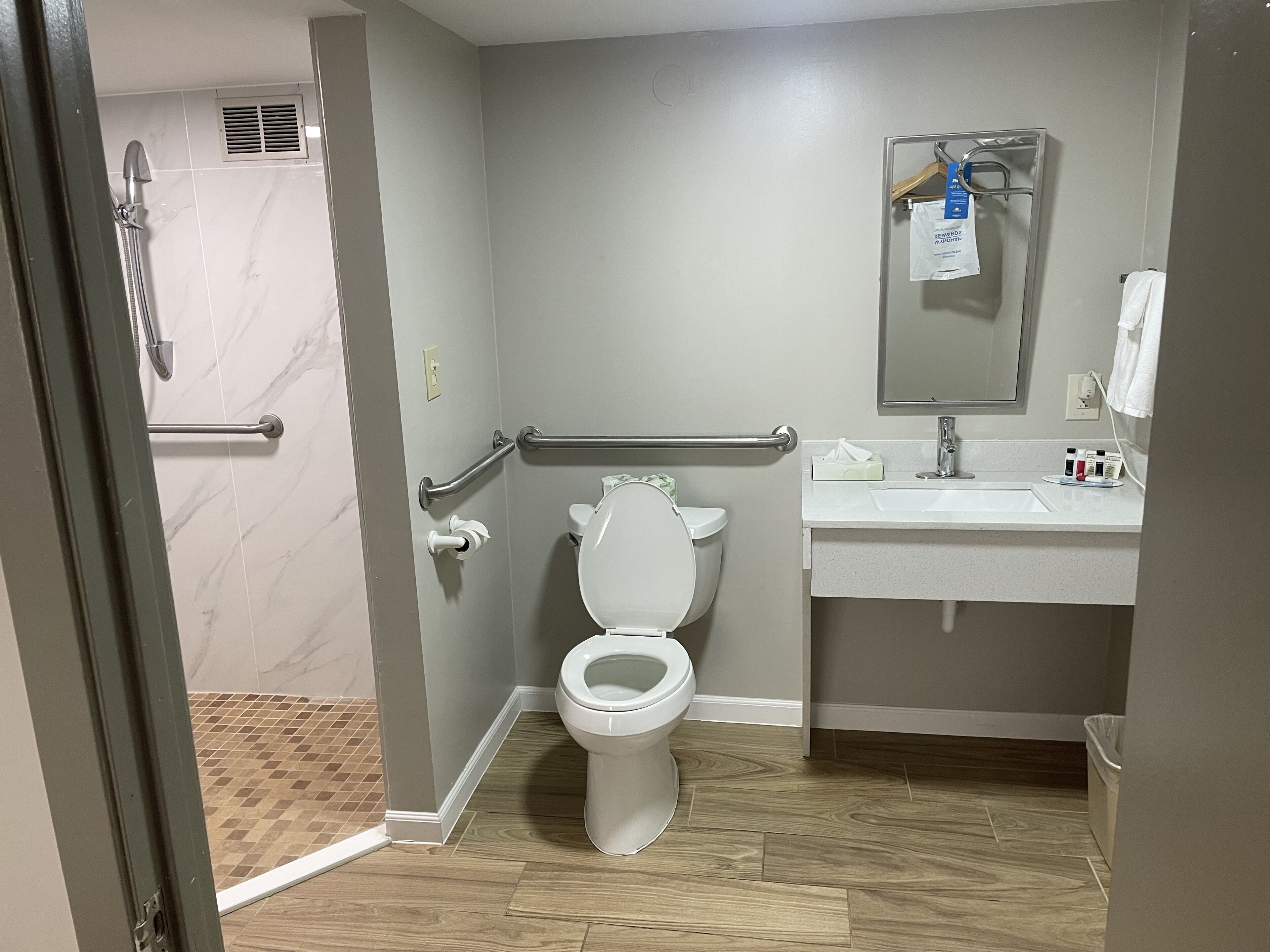 A bathroom with a toilet, sink, mirror, and shower.