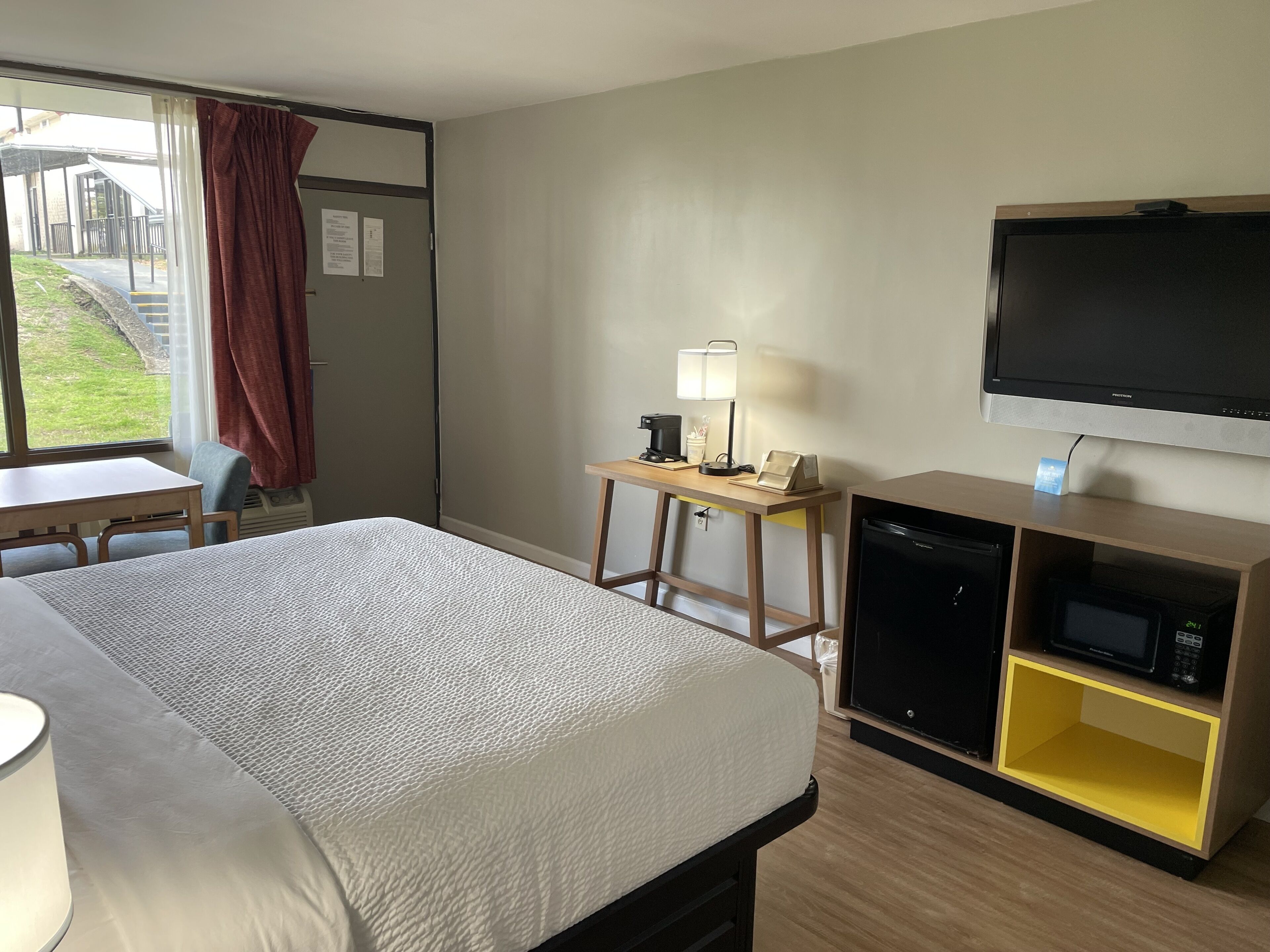 A hotel room with a bed, a desk, a television, a microwave, and a small table with a lamp.