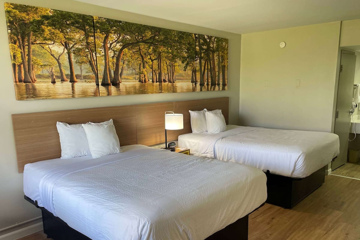 Ein Hotelzimmer mit zwei Betten, einem großen Baumgemälde und einem hölzernen Kopfteil.
