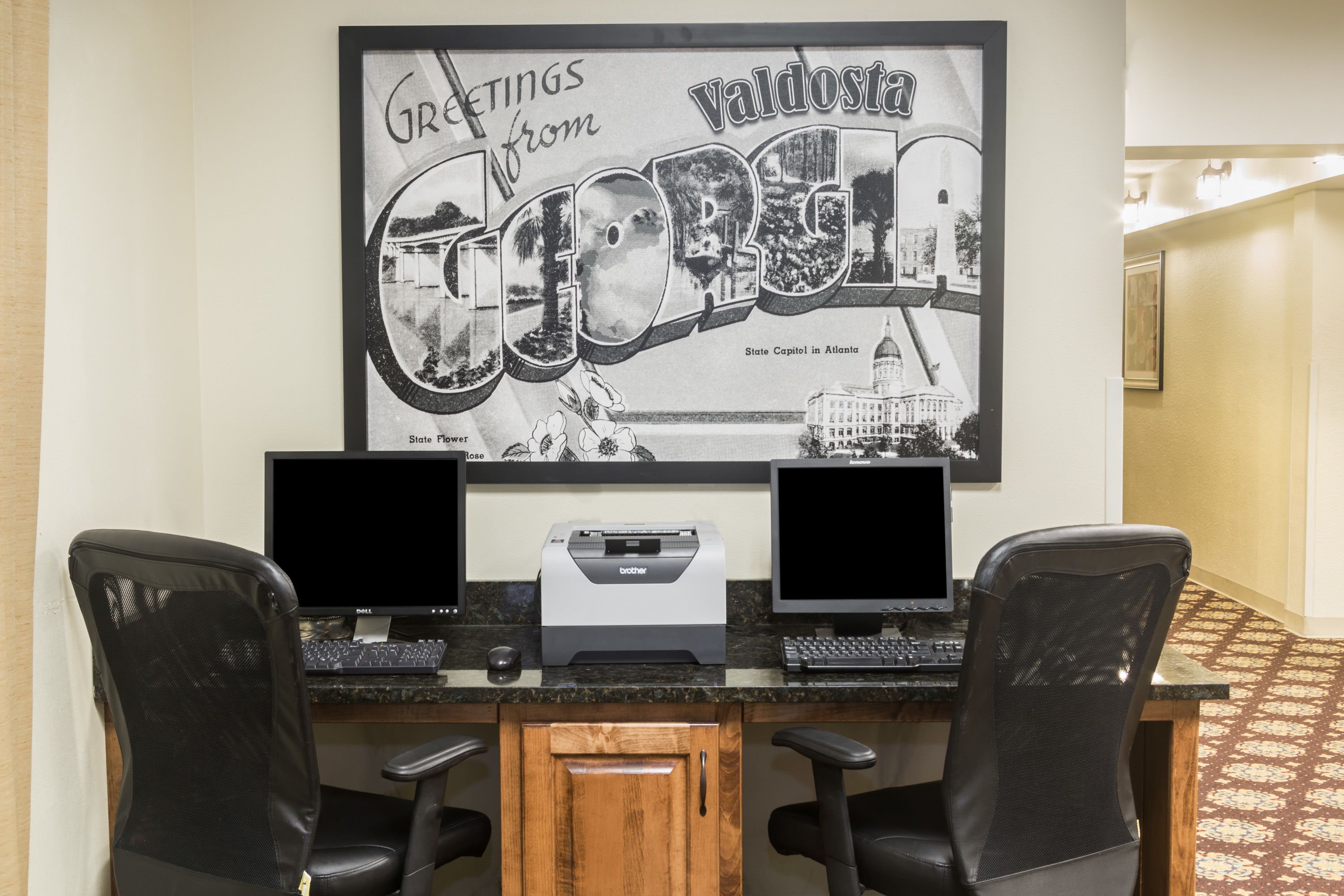 Een werkplek met twee monitoren, een Brother-printer en twee zwarte stoelen met mesh-rug.