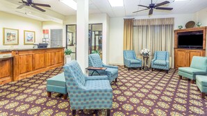 A hotel lobby with patterned carpet, blue armchairs, a wooden reception desk, ceiling fans, and a television. - Days Inn by Wyndham Valdosta/Near Valdosta Mall (Valdosta)