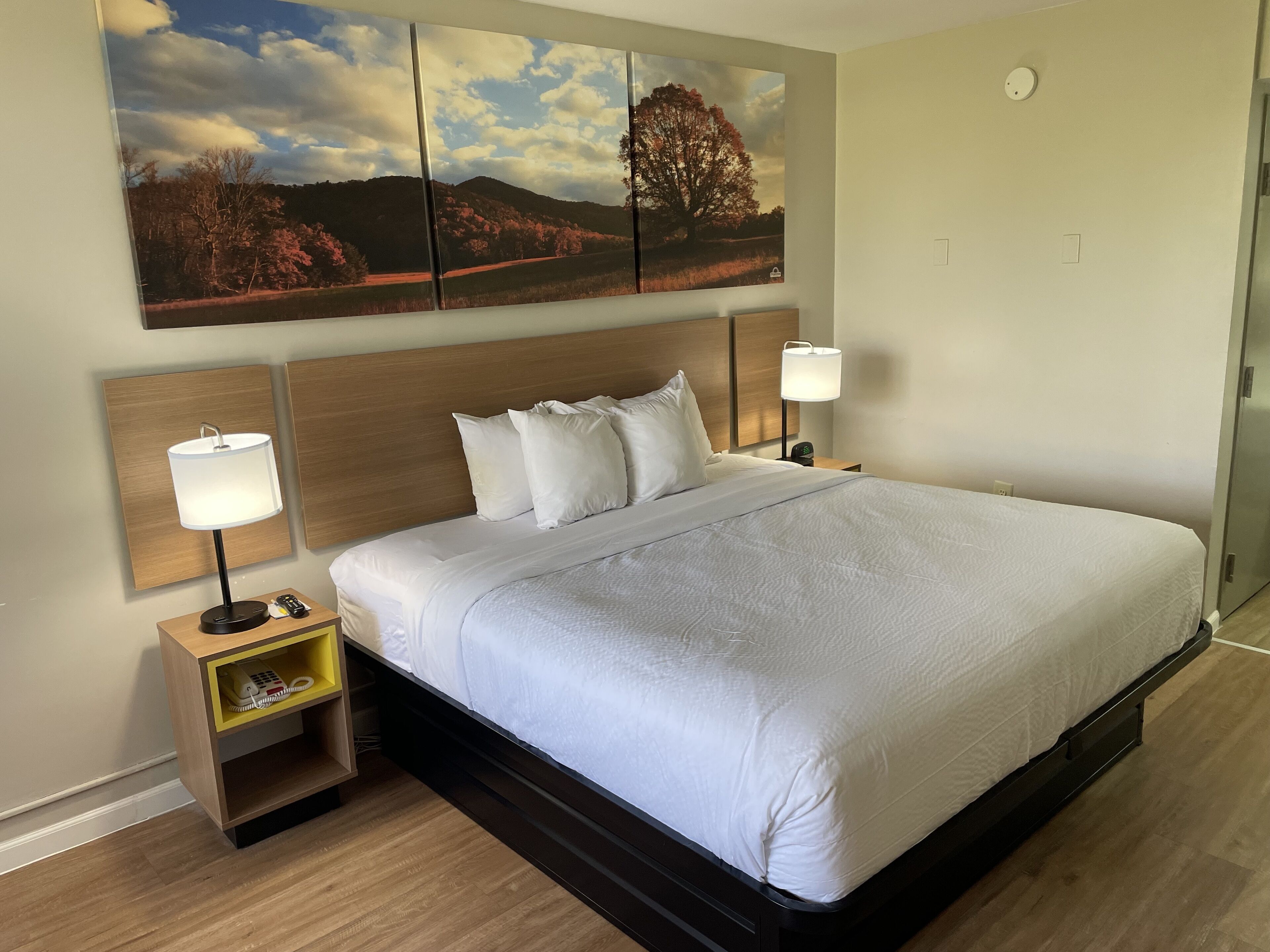 A neatly made bed with white linens, a wooden headboard, and two bedside lamps.