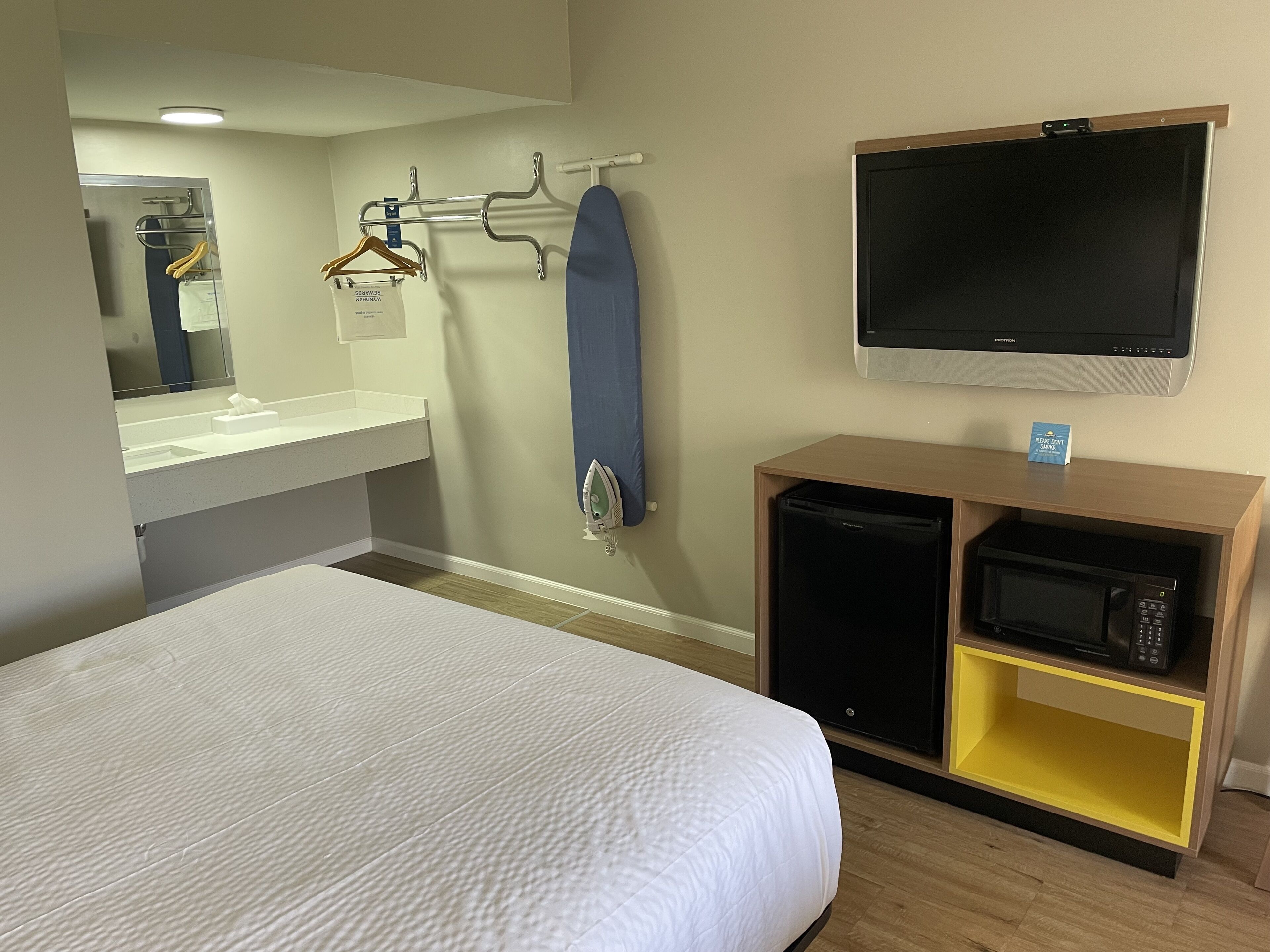 Hotelkamer met een bed, een klein kitchenette, een spiegel, een kledingrek en een televisie.