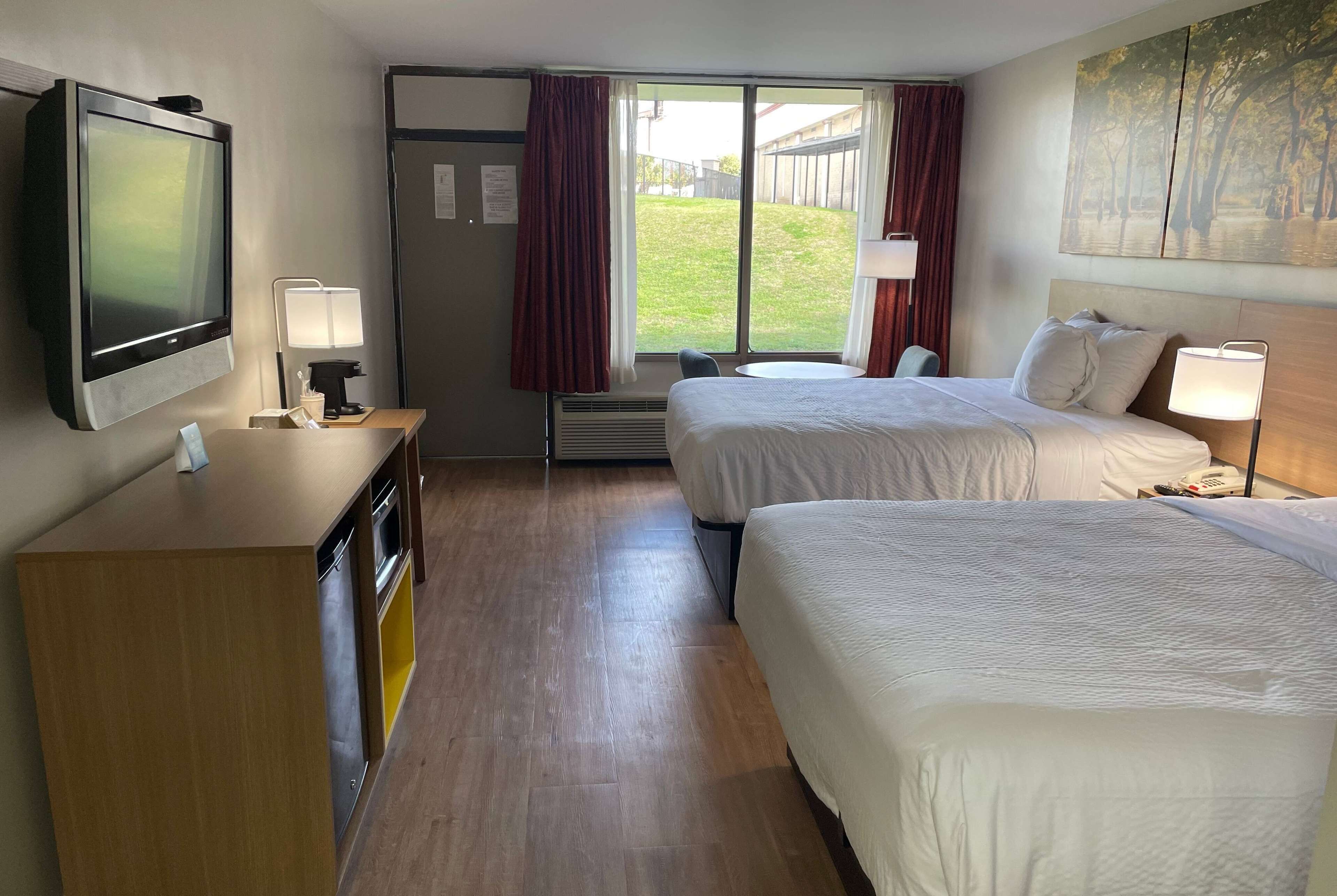 A hotel room with two beds, a TV, a desk, and a window with curtains.