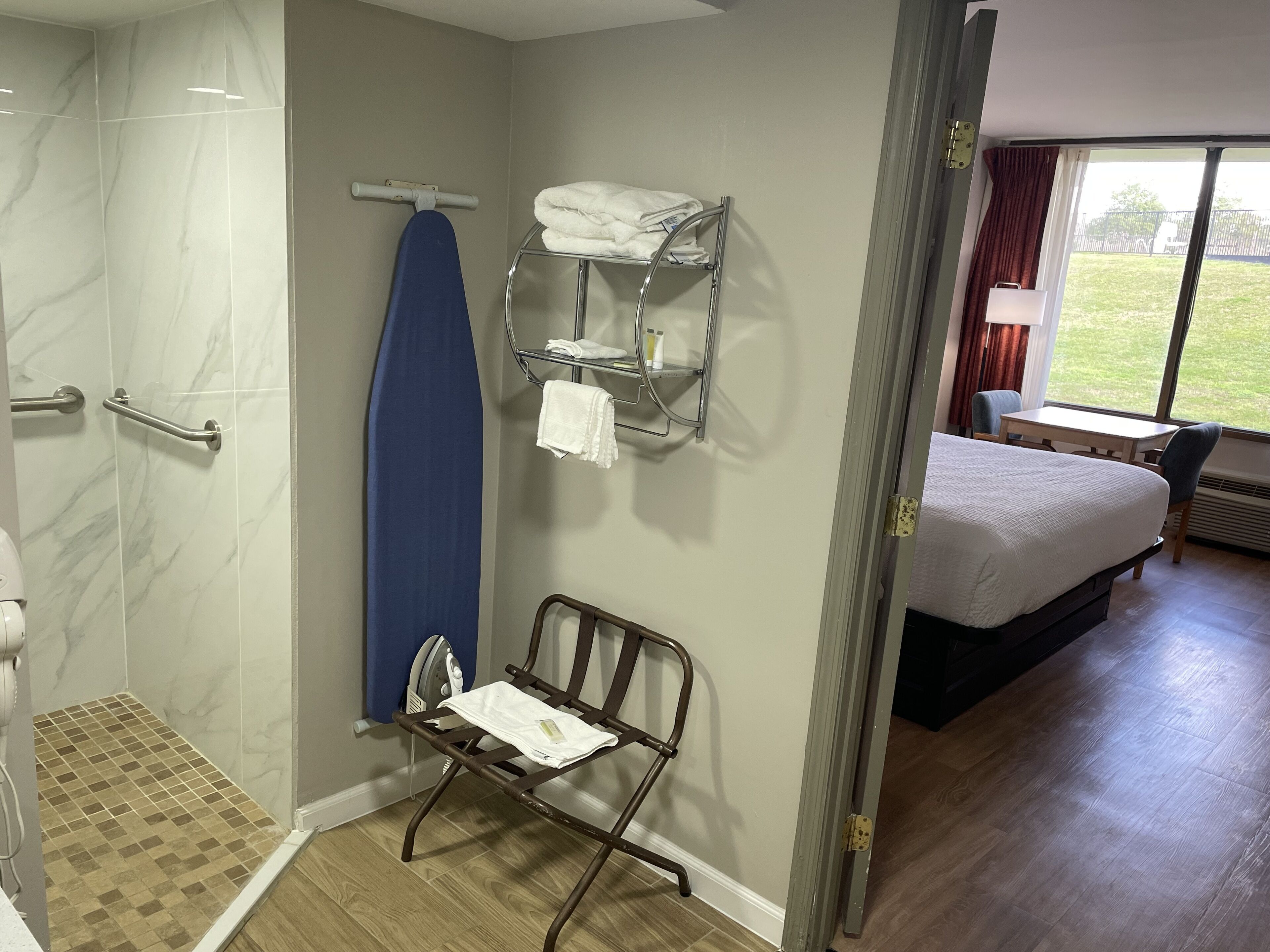 A hotel room with a shower, a drying rack, a bed, a small table, and a window with a view of the outdoors.