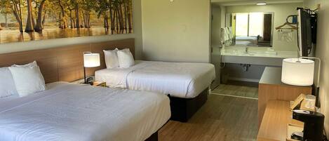 A hotel room with two beds, a large mirror, a small table with a coffee maker, and a painting of trees on the wall.