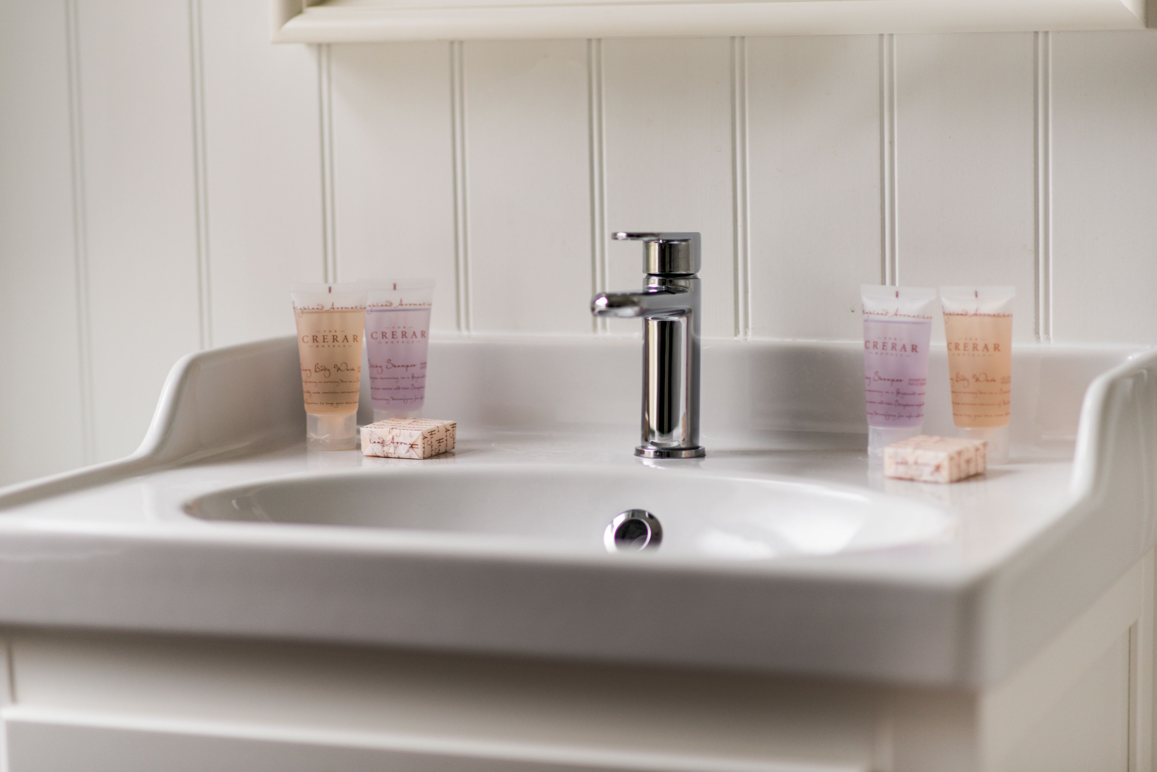 A bathroom sink with a chrome faucet and two bottles of 'CREAR' soap on the counter.