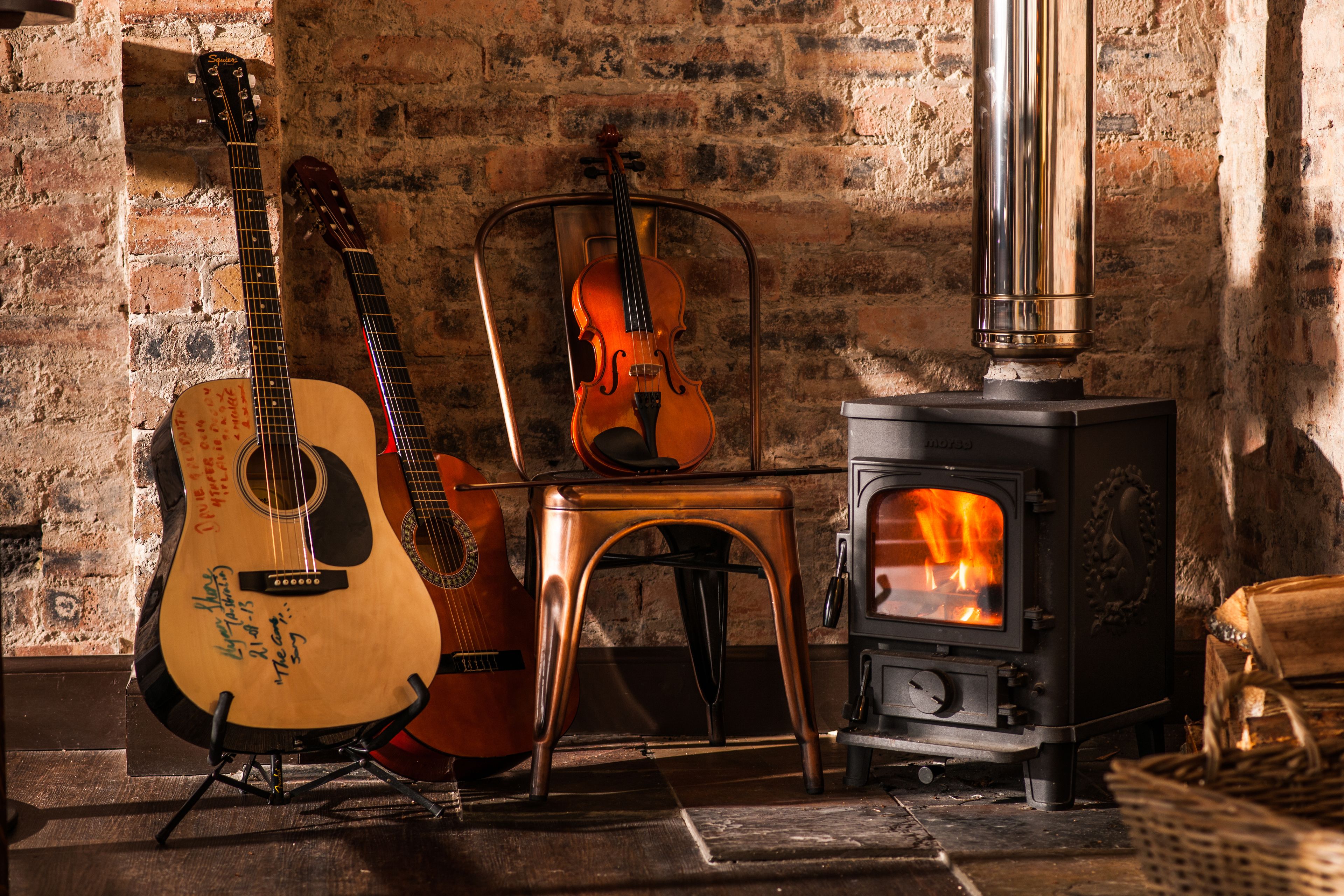 A rustic room with a wood-burning stove, a violin, and a guitar.