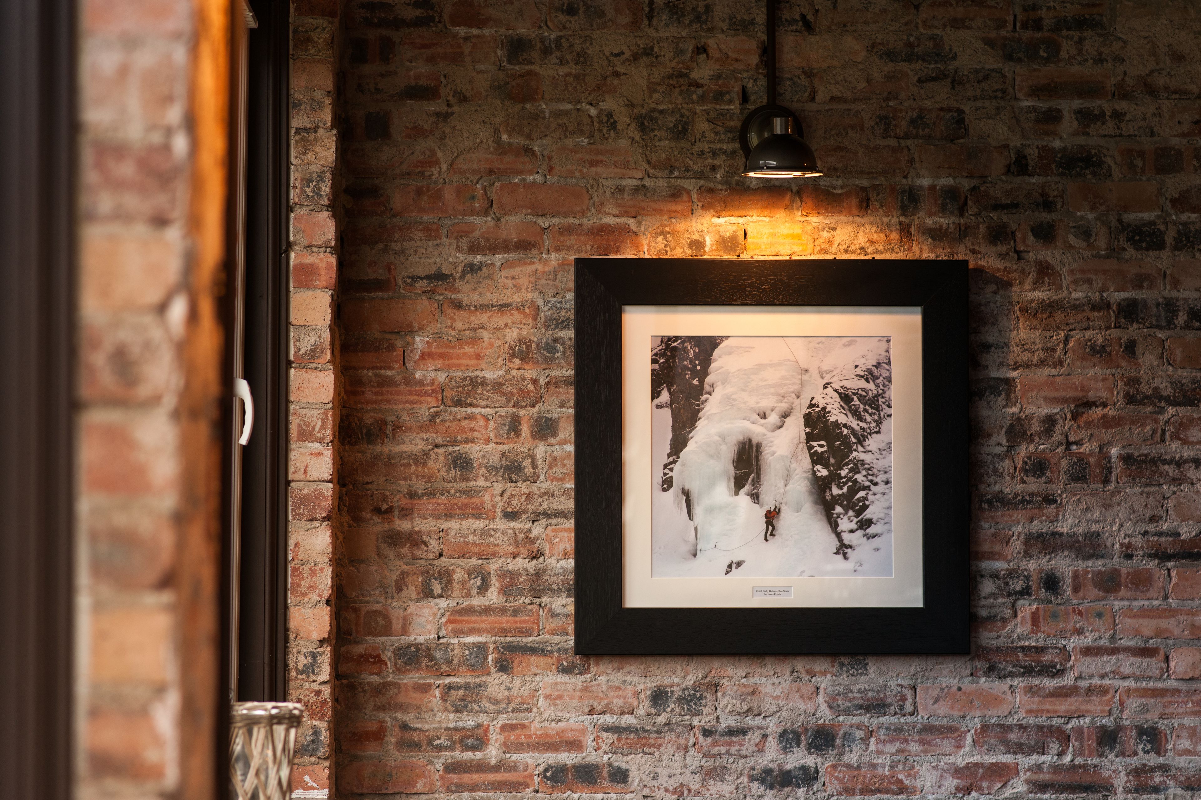 A framed photograph on a brick wall with a hanging light fixture above it.