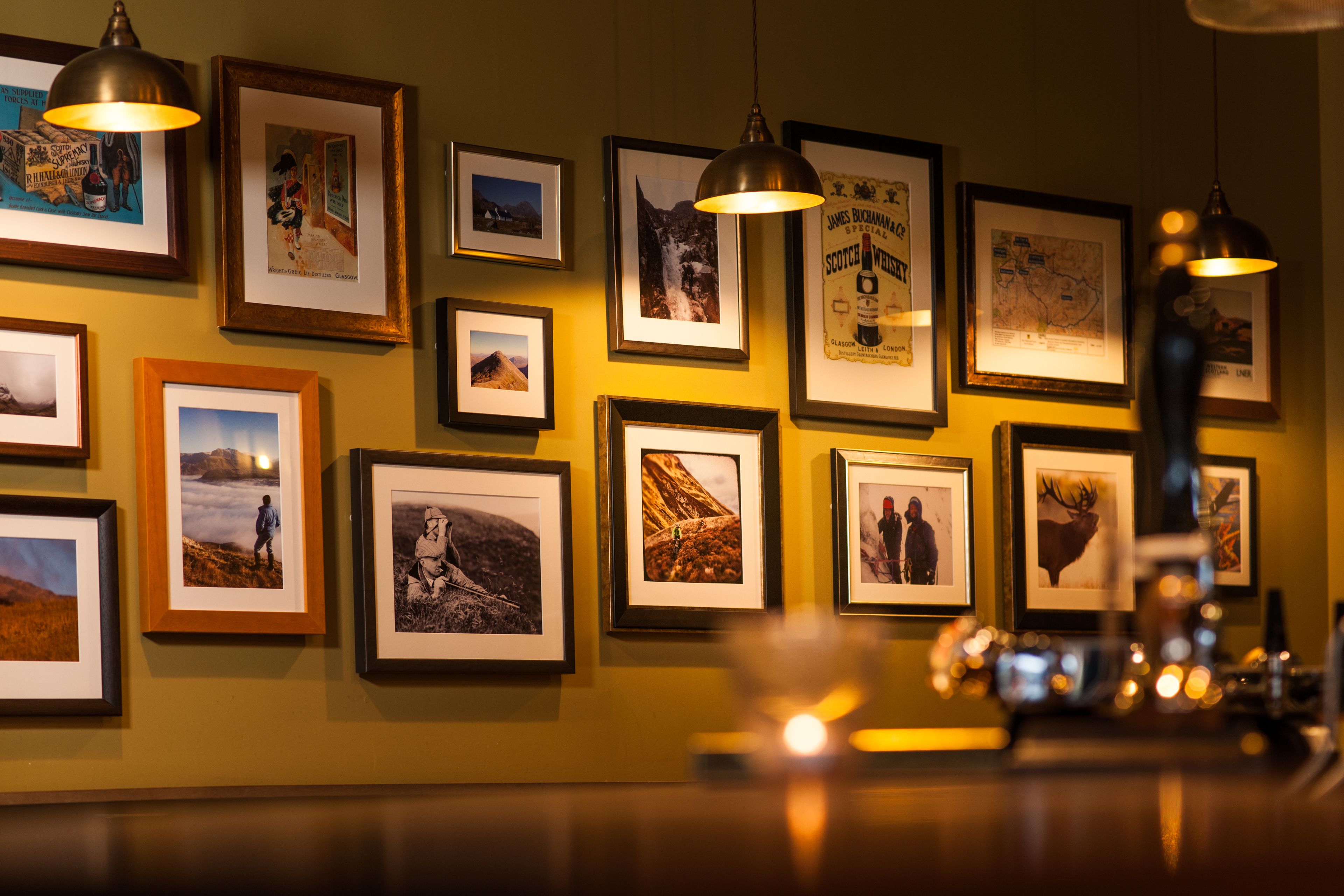 A wall with multiple framed photographs, some with text, and two hanging pendant lights.
