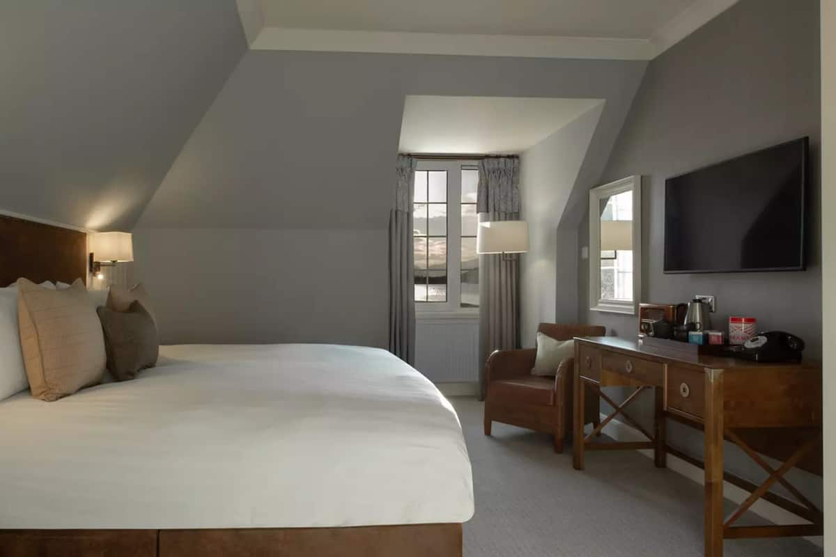 A bedroom with a large bed, a desk, a chair, a TV, and a window with curtains.