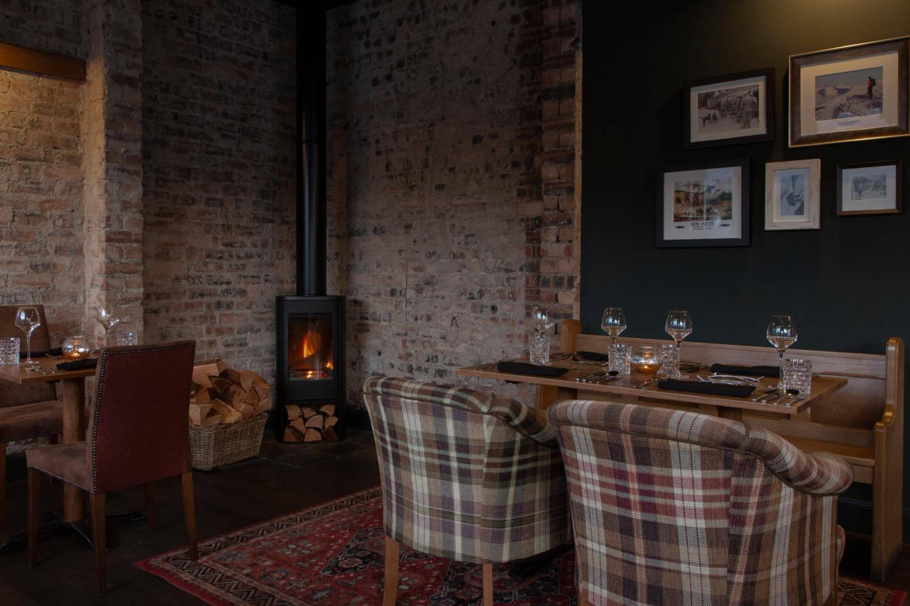 Una habitación acogedora con pared de ladrillo, chimenea y una mesa de comedor para dos con sillas a cuadros.