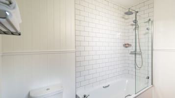 Une salle de bain avec des murs recouverts de carreaux blancs, une douche à parois de verre et une baignoire blanche.