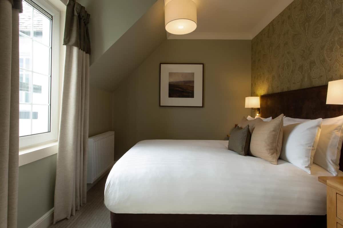 A neatly made bed with a headboard, a framed picture on the wall, and a window with curtains.