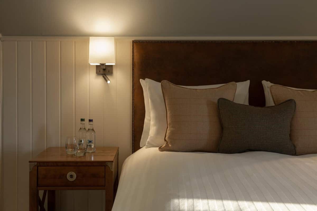 A neatly made bed with a wooden headboard, a bedside table with a lamp, and two bottles on the table.