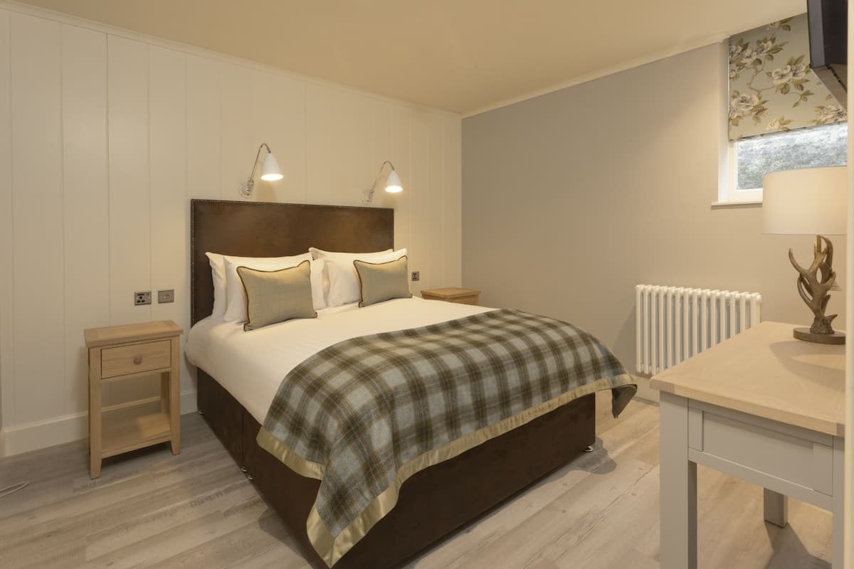 A bedroom with a bed, bedside tables, a lamp, a radiator, and a window with curtains.
