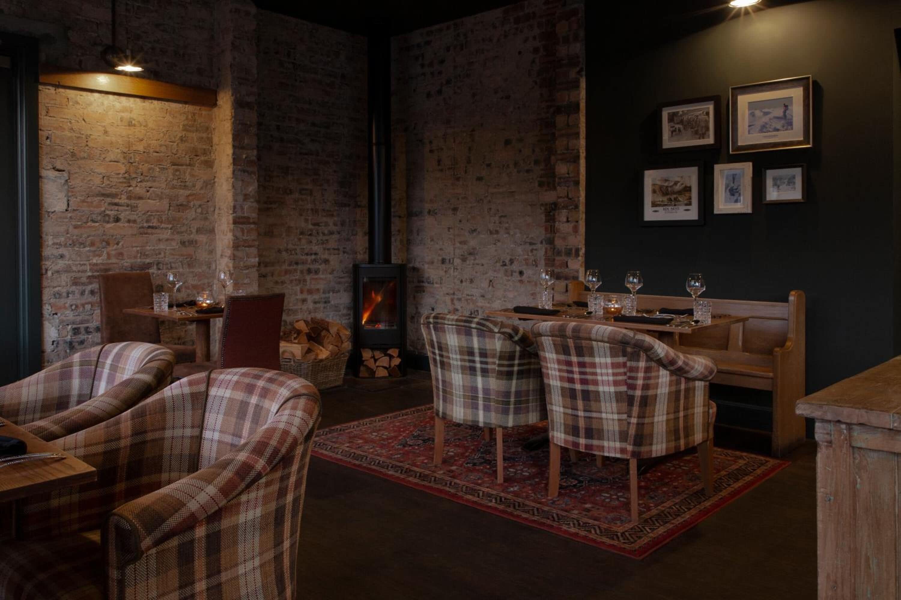 A cozy room with a brick wall, a fireplace, plaid chairs, and a table set for dining.