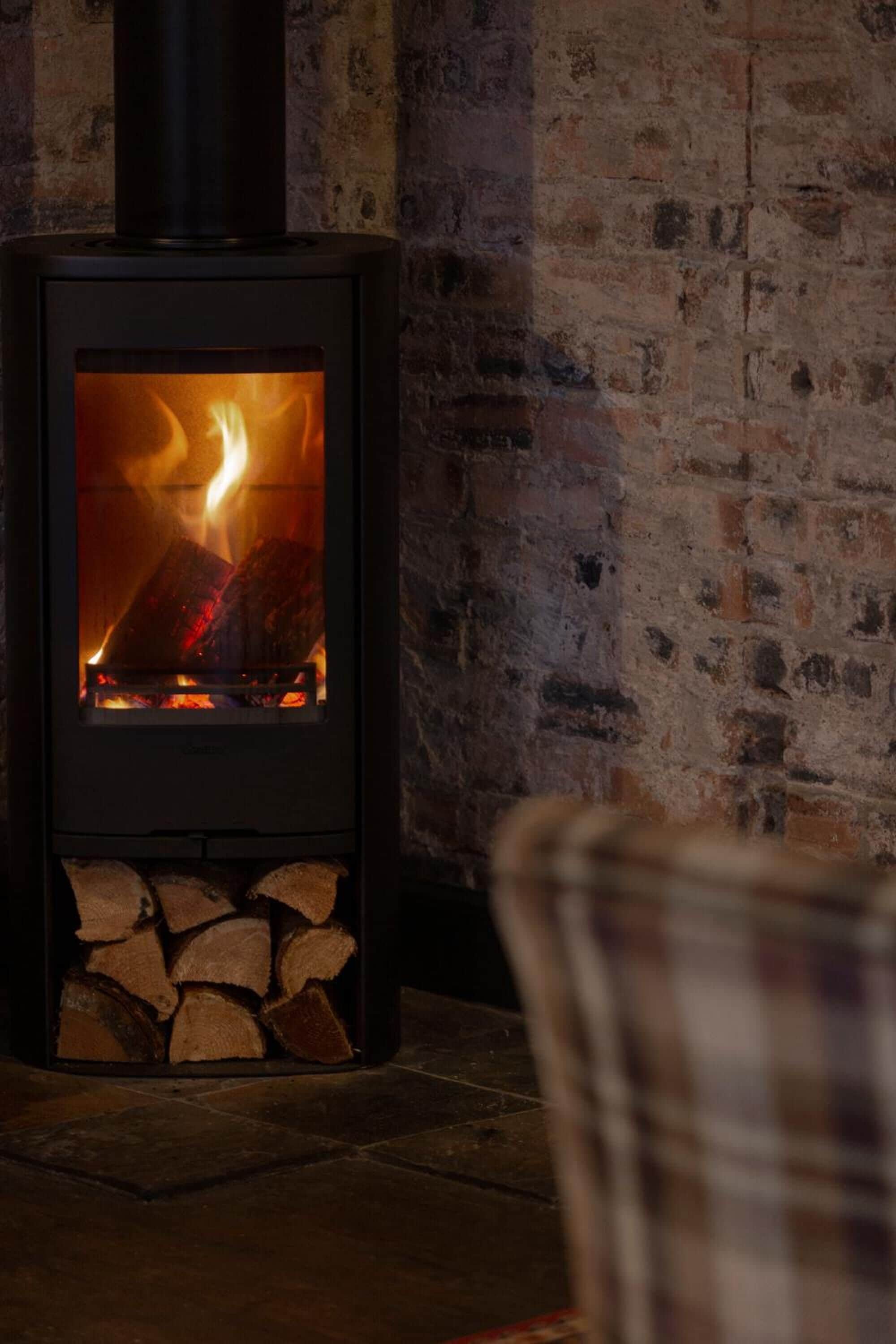 A wood-burning stove with a visible fire, set against a brick wall.
