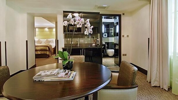 A modern hotel room with a round dining table, comfortable seating, a large mirror, and a decorative orchid arrangement. - Montcalm Brewery Townhouse (London)