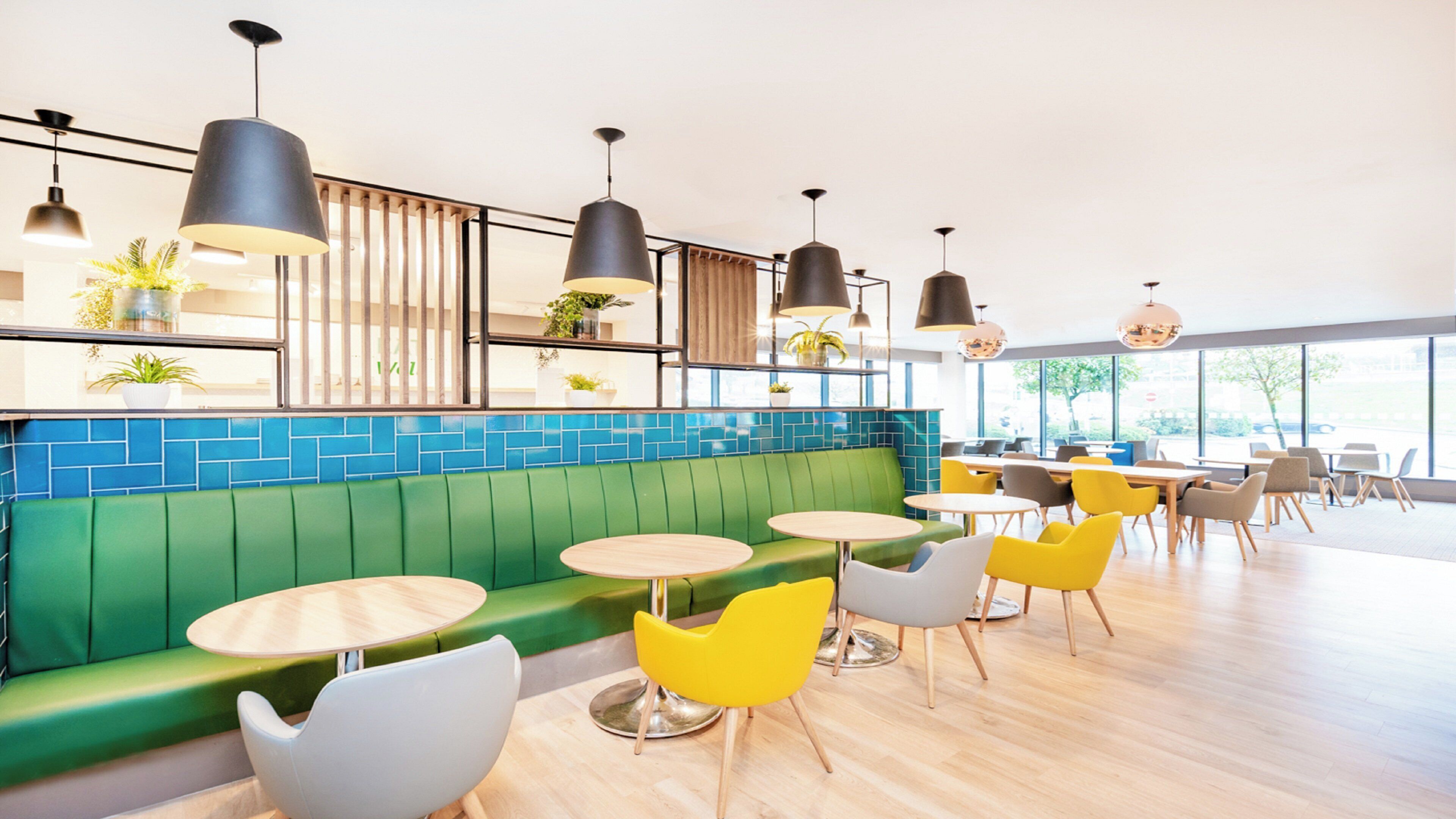 A modern cafe interior with green seating, yellow chairs, and multiple tables.
