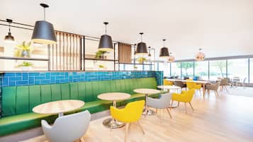 A modern cafe interior with green seating, yellow chairs, and multiple tables.