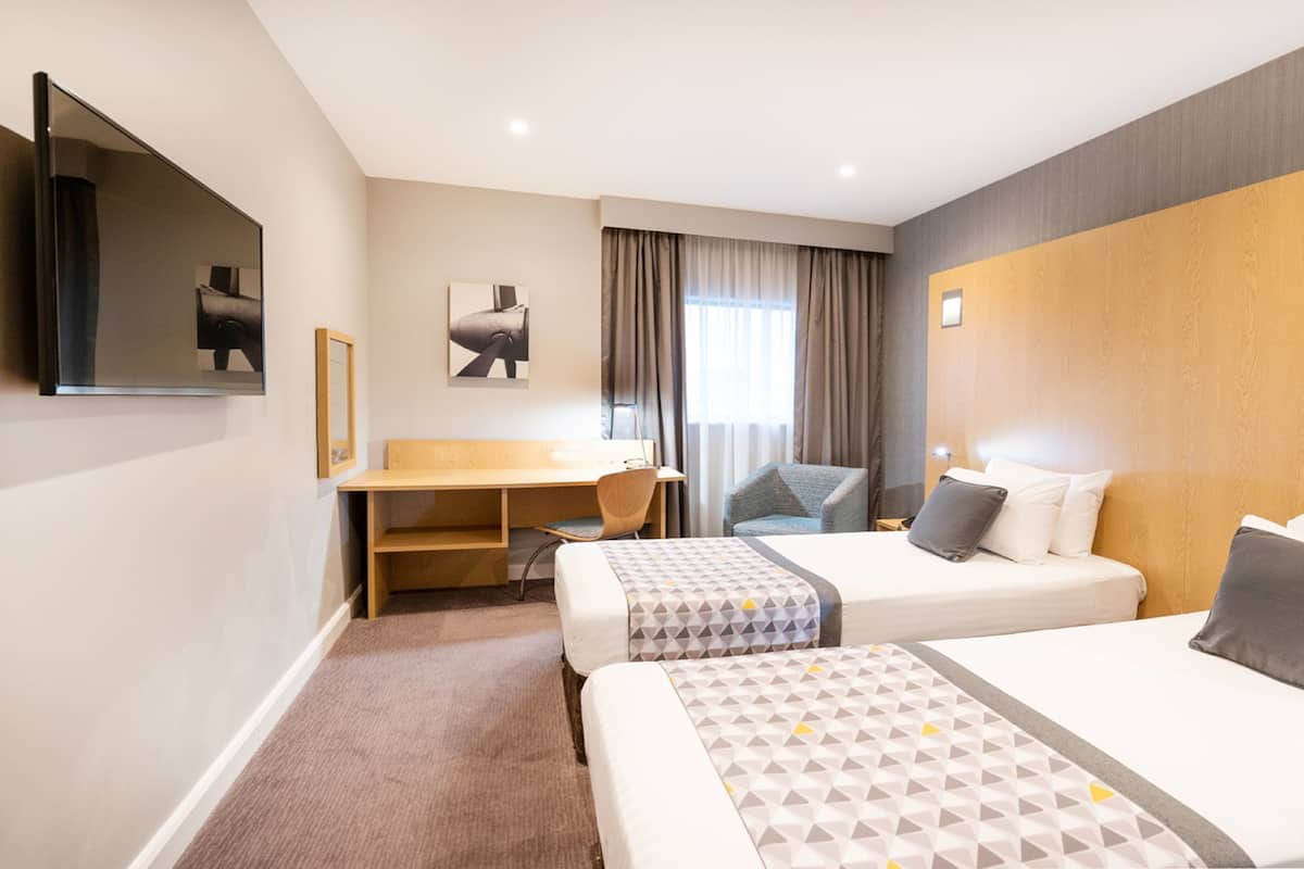 A hotel room with two beds, a desk, a chair, a TV, and a window with curtains.