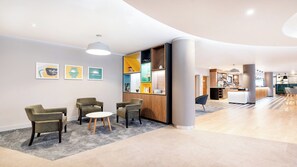 Un hall d’hôtel moderne avec un comptoir d’accueil, un espace salon et des œuvres d’art accrochées aux murs.