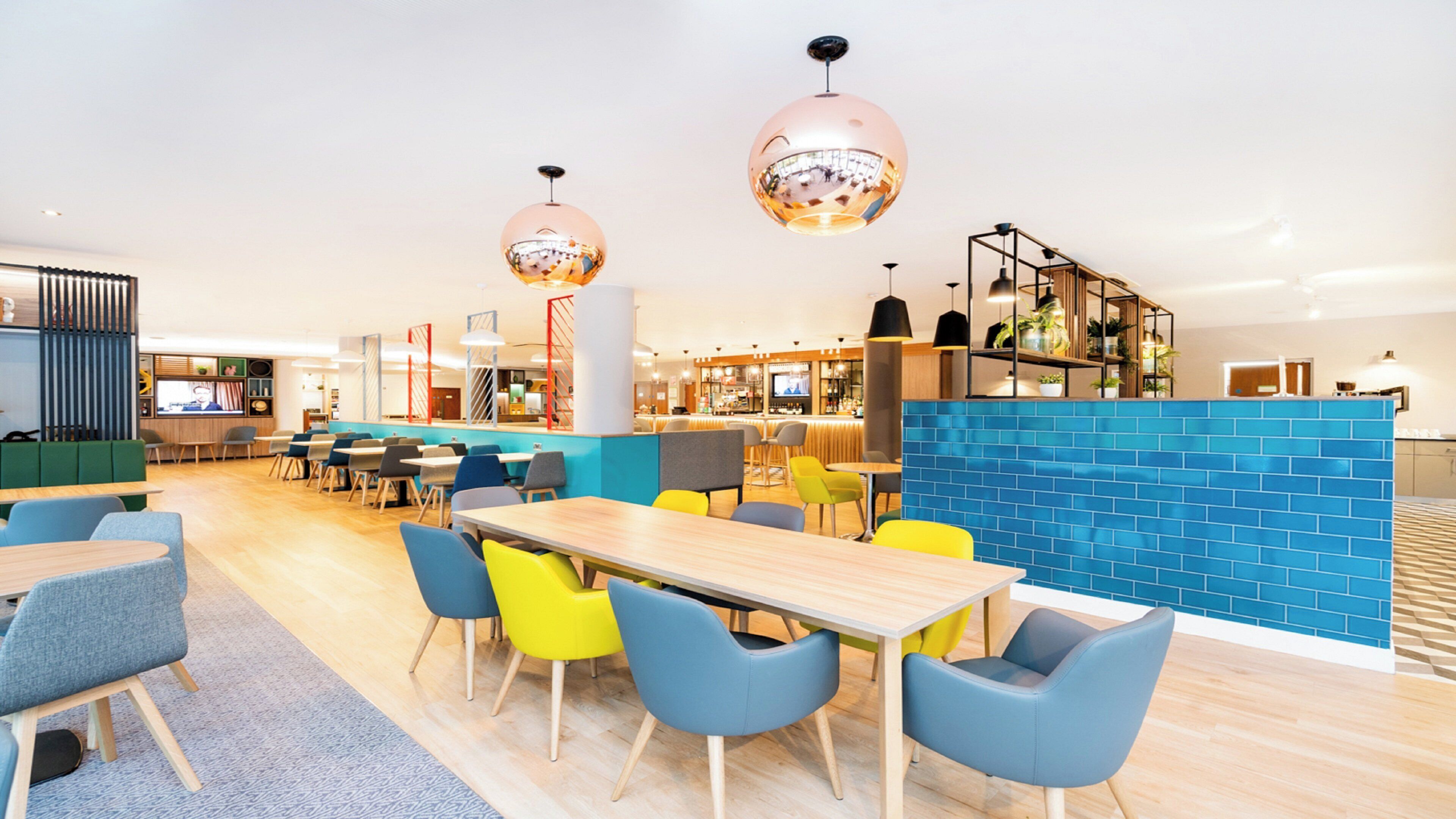 Un restaurante moderno con una zona de bar, mesas de madera y sillas coloridas.