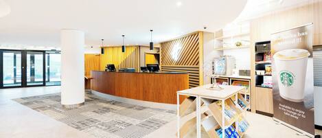 Un hall d’hôtel moderne avec un comptoir d’accueil, un espace café et une vue sur l’extérieur.