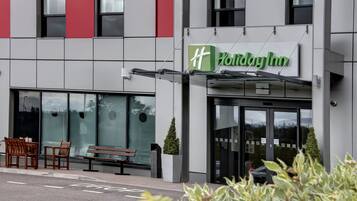 Entrada de un hotel Holiday Inn con un banco fuera y una vista despejada de la fachada del edificio.