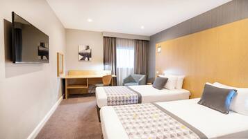 A hotel room with two beds, a desk, a chair, a TV, and a window with curtains.