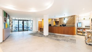A spacious lobby with a reception desk, a large pillar, and a view through the glass doors.
