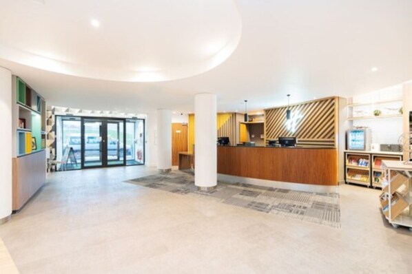 A spacious lobby with a reception desk, a large pillar, and a view through the glass doors. - Holiday Inn London - Luton Airport by IHG (Luton)