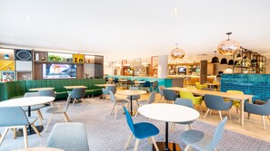 Un espace lounge moderne avec des sièges verts, des tables rondes et un bar dont le mur arrière est recouvert de carreaux bleus.