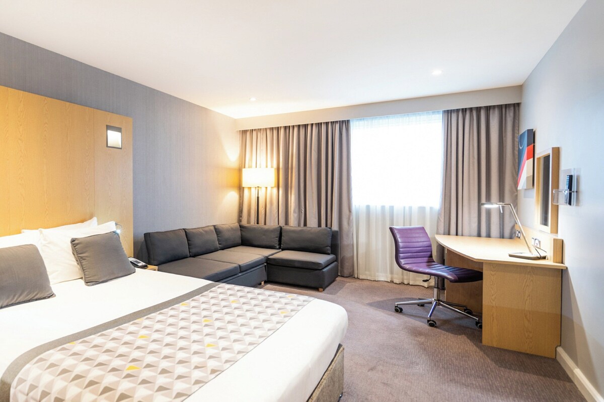A hotel room with a large bed, a sofa, a desk, and a chair.
