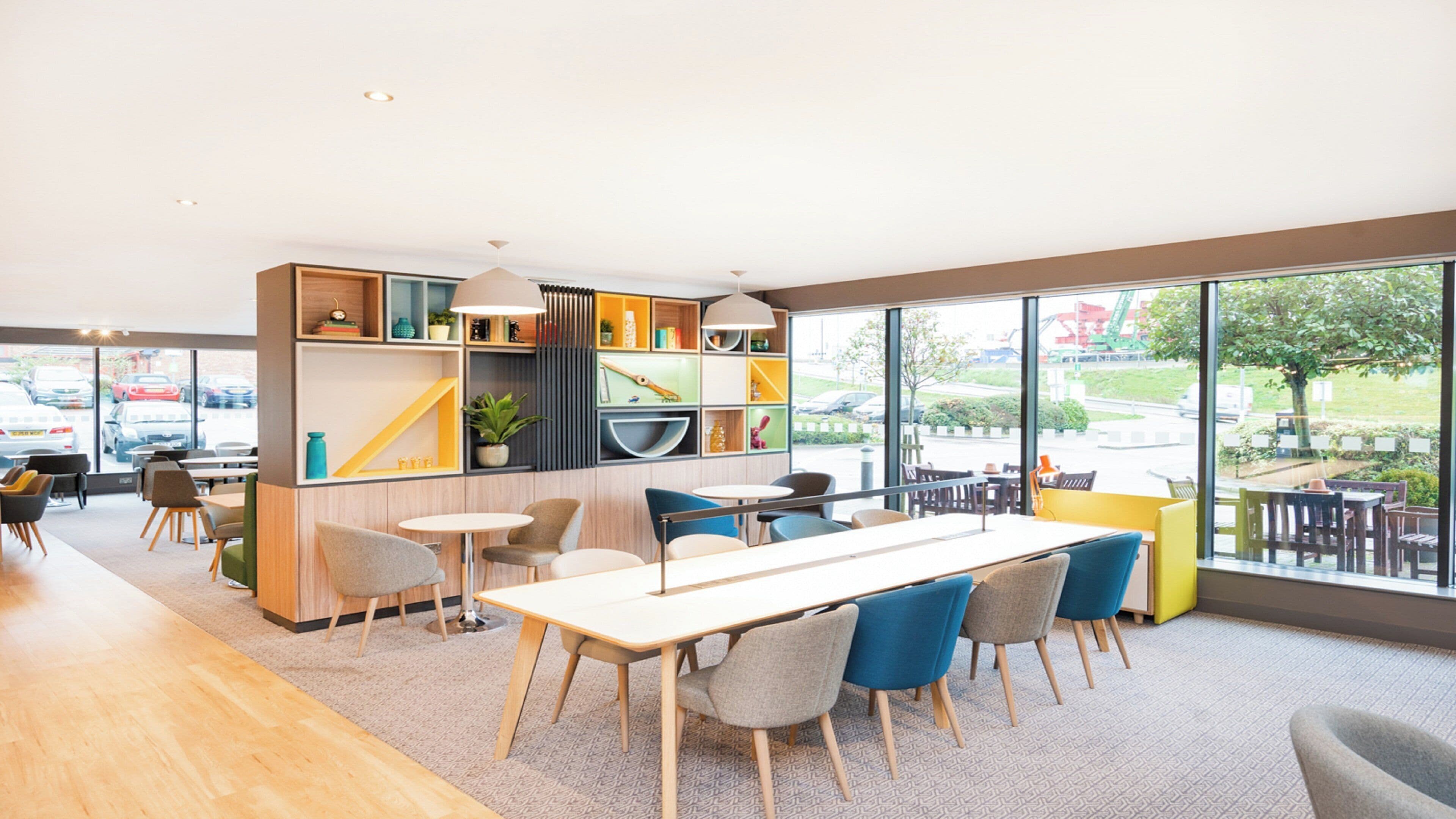 A modern interior with a dining area, a bookshelf, and large windows offering a view of the outdoors.