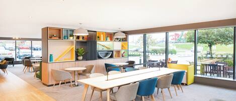 A modern interior with a dining area, a bookshelf, and large windows offering a view of the outdoors.